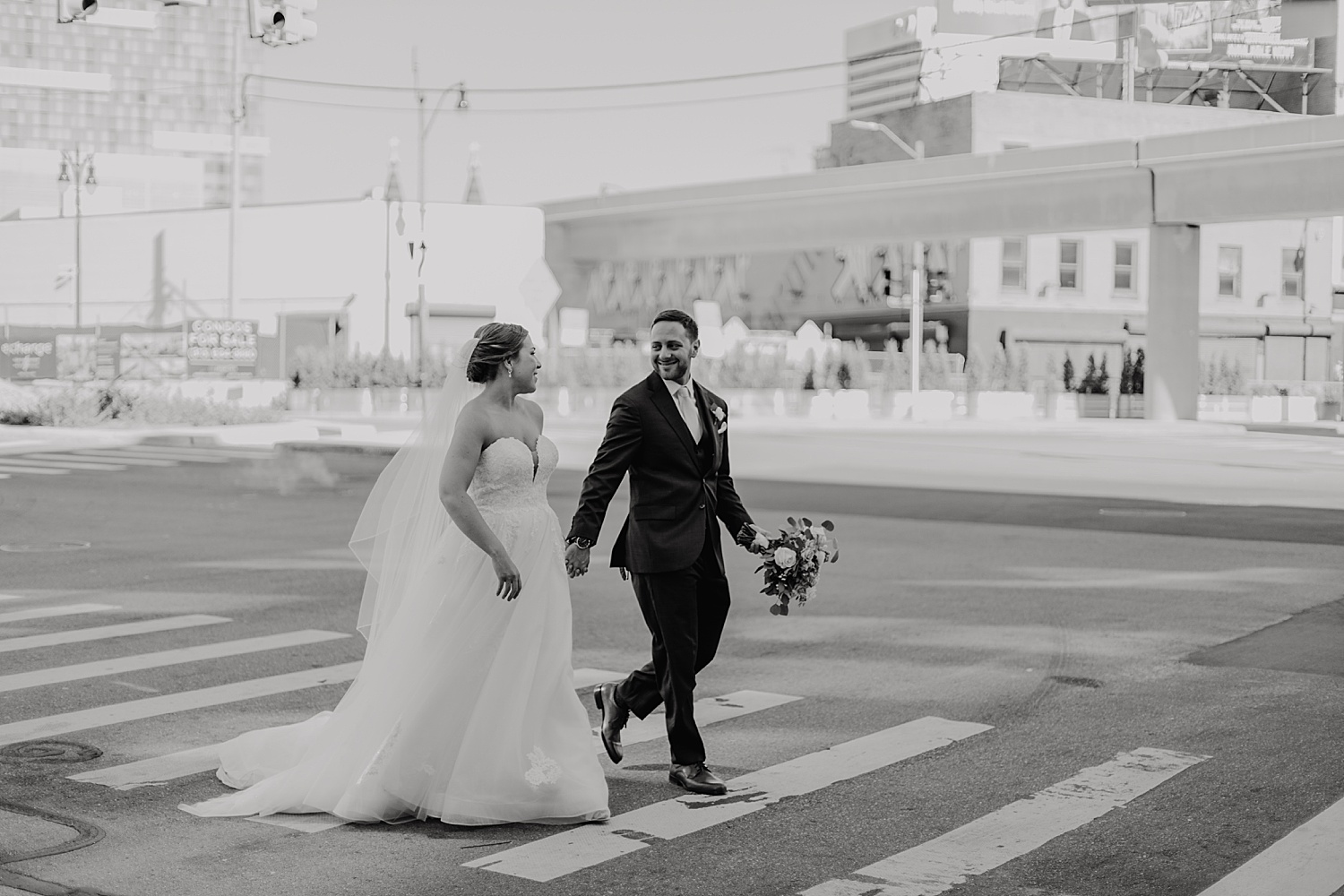 bride and groom walk downtown Detroit at ford piquette plant while holding hands 