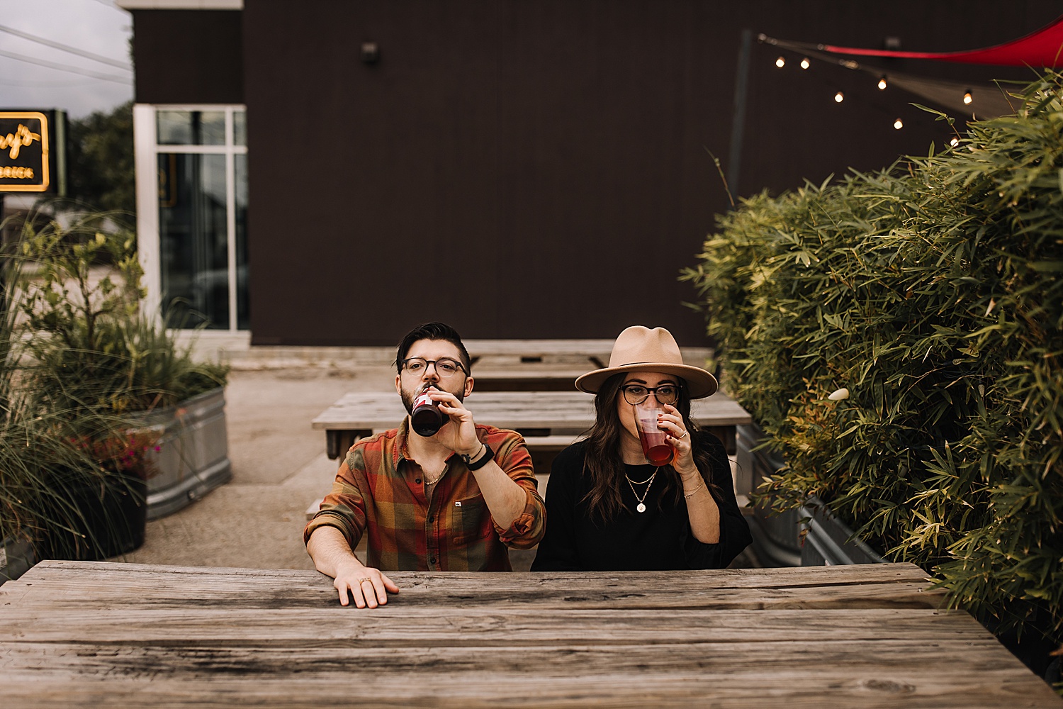 engaged couple drinks beer while sitting at table of brewery with Detroit engagement photographer 
