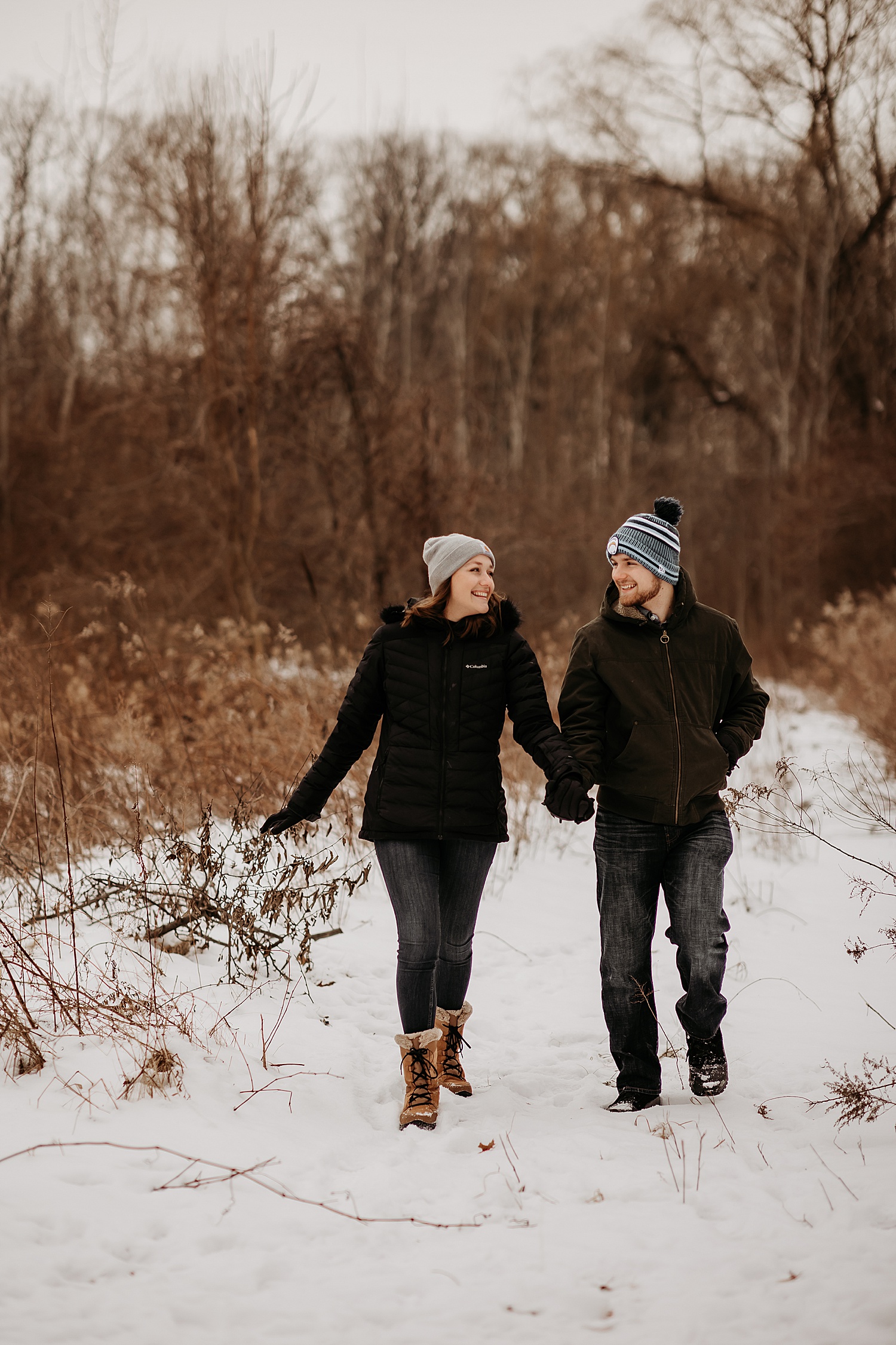 Engaged couple wearing winter coats and beanies during snowy engagement session