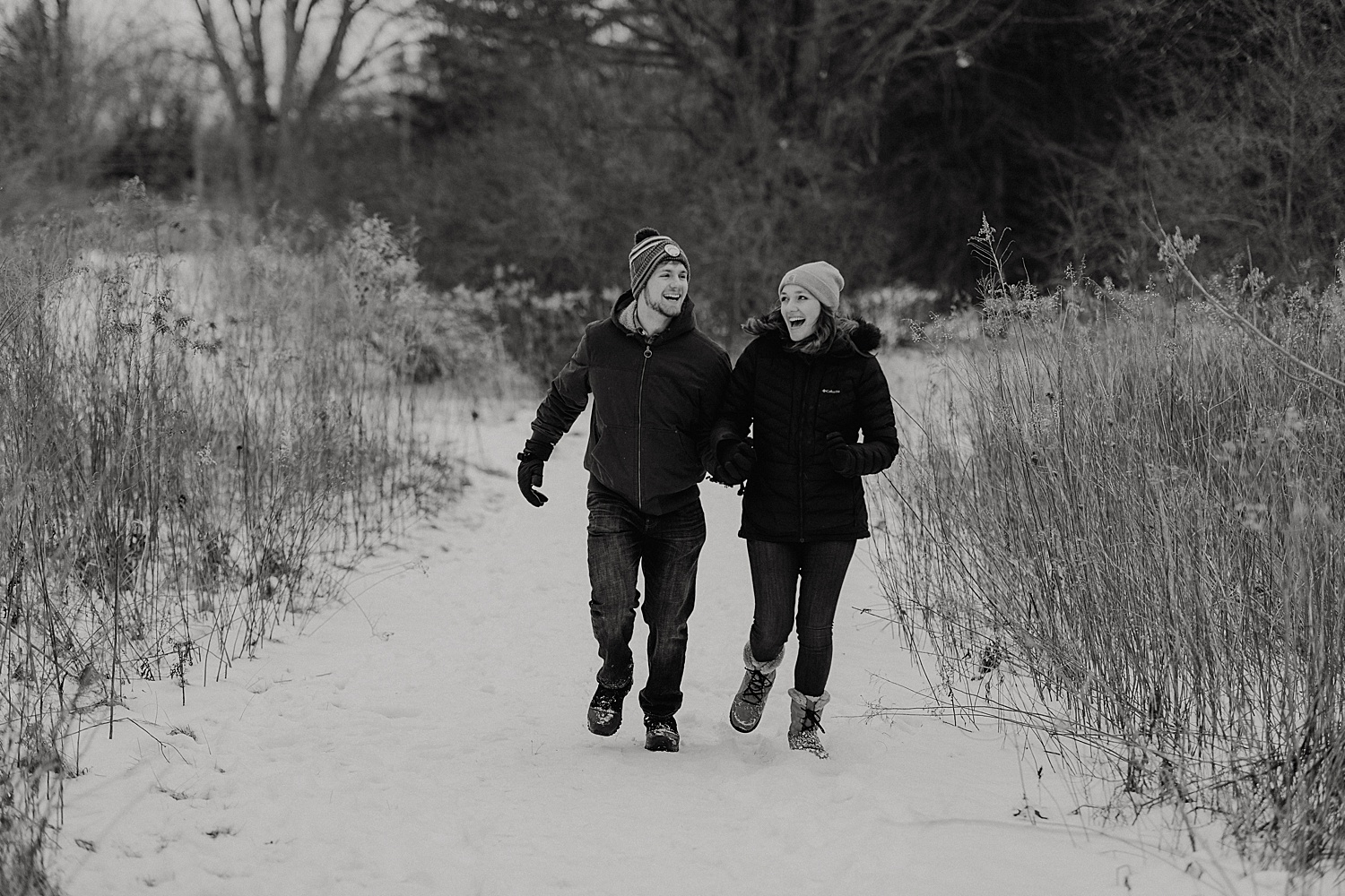 Engaged couple running on a snow path with Michigan engagement photographer