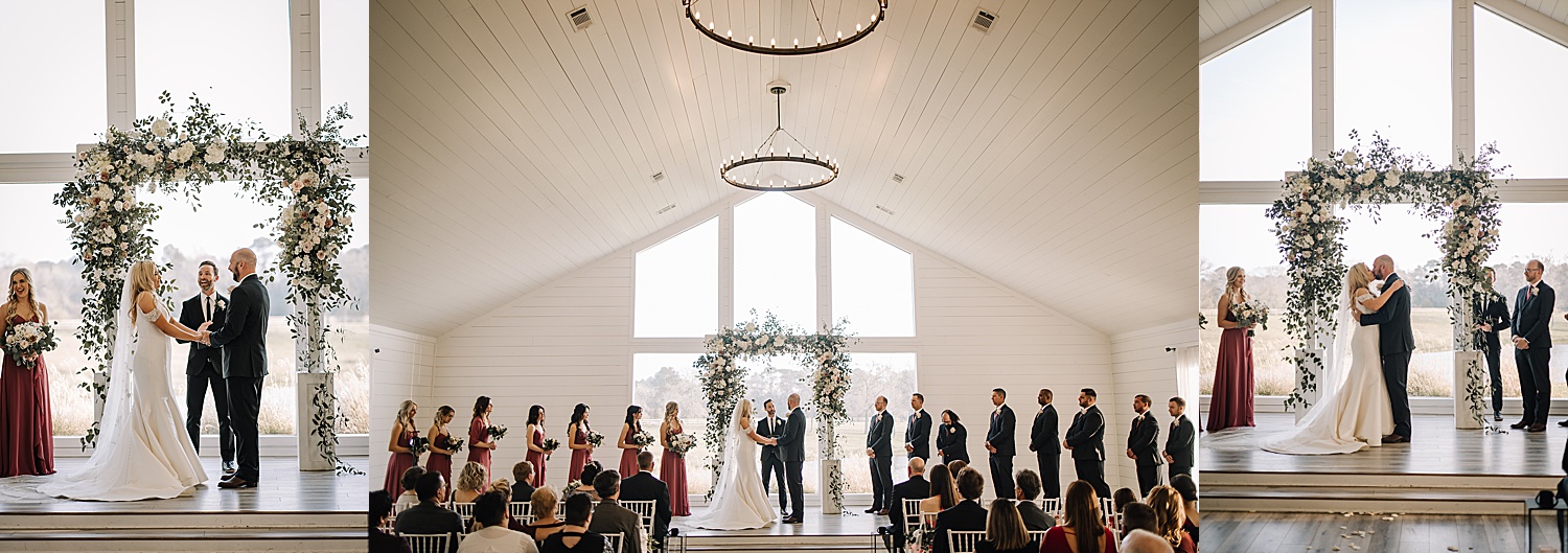 Bride and groom share first kiss during ceremony in classy white event barn 